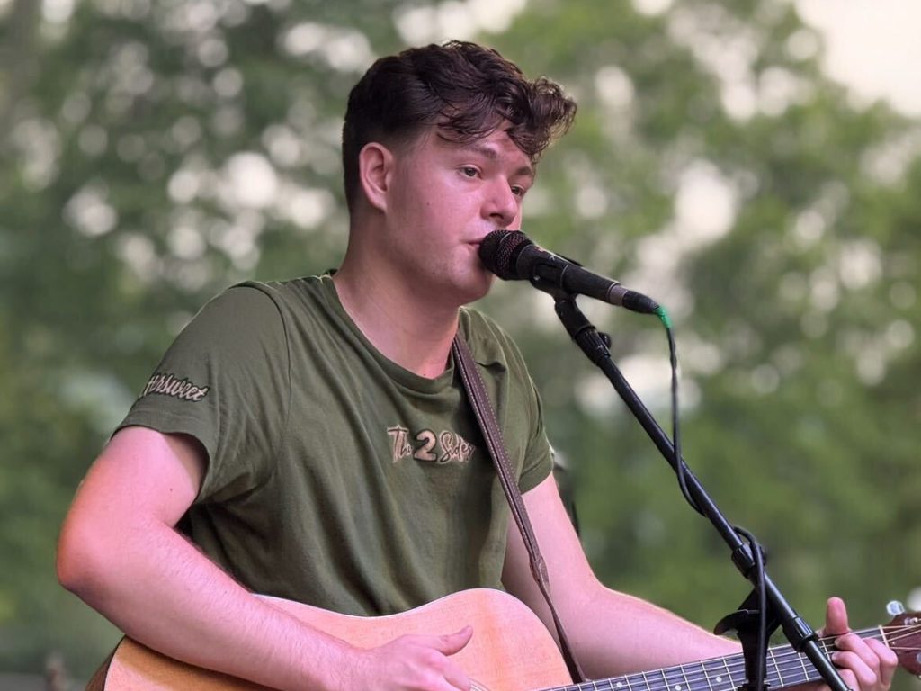 Christian Teets Playing the Guitar on a Stage Outside